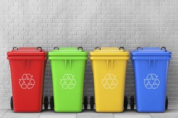Four recycling bins in a row in front of a brick wall
